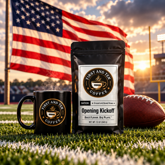 A black coffee pouch labeled 'FIRST AND TEN COFFEE' and a matching black mug sit on grass at a football stadium, with an American flag, football, and sunset sky in the background.